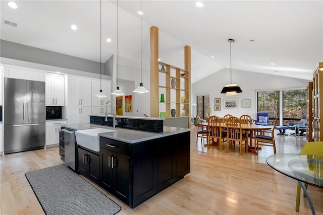 kitchen with pendant lighting, light stone counters, built in fridge, and a center island with sink