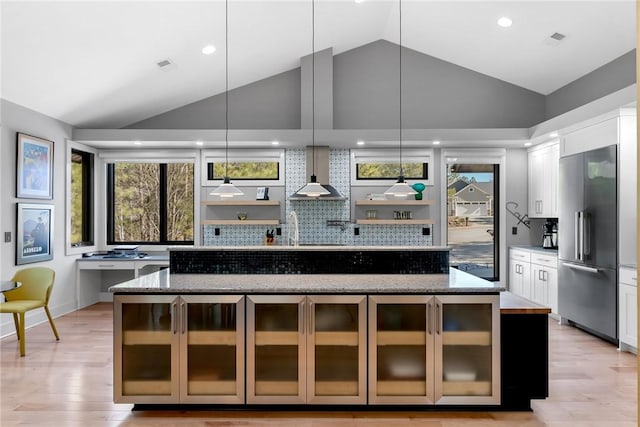 kitchen featuring stainless steel built in refrigerator, light stone countertops, wall chimney range hood, and white cabinets