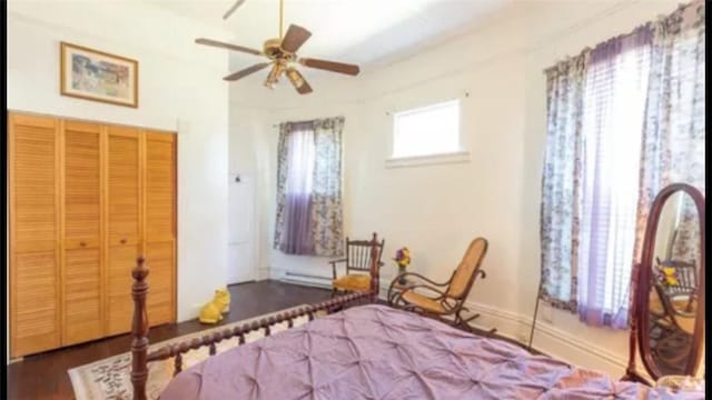 bedroom with a baseboard radiator, dark wood-type flooring, ceiling fan, and a closet