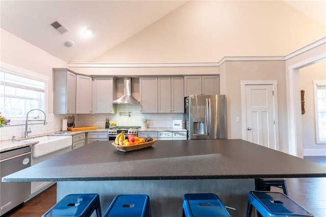 kitchen with sink, a breakfast bar area, stainless steel appliances, a kitchen island, and wall chimney exhaust hood