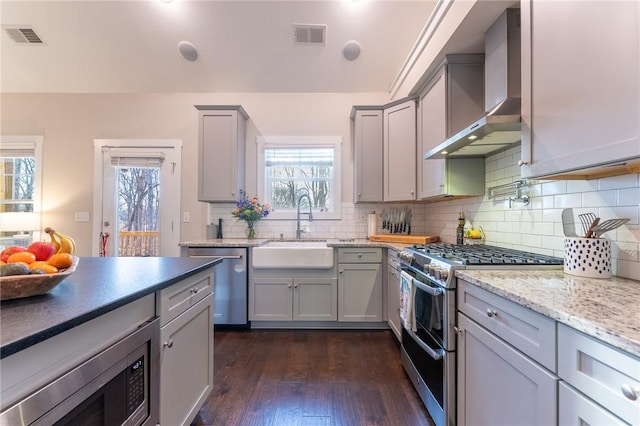 kitchen with gray cabinetry, appliances with stainless steel finishes, sink, and wall chimney range hood