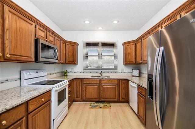 kitchen featuring light stone counters, sink, light hardwood / wood-style floors, and appliances with stainless steel finishes