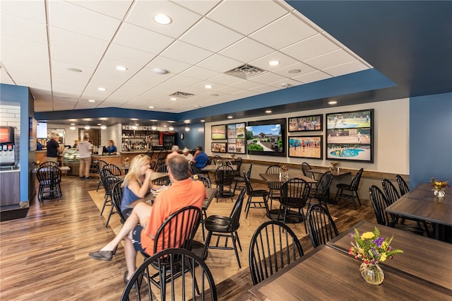 dining space featuring a drop ceiling, hardwood / wood-style floors, and bar area