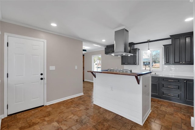 kitchen with pendant lighting, sink, island exhaust hood, ornamental molding, and a kitchen bar