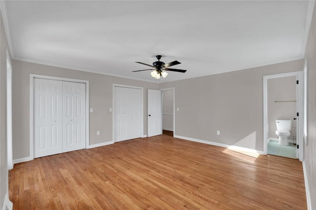 unfurnished bedroom featuring crown molding, light hardwood / wood-style flooring, ensuite bath, ceiling fan, and multiple closets