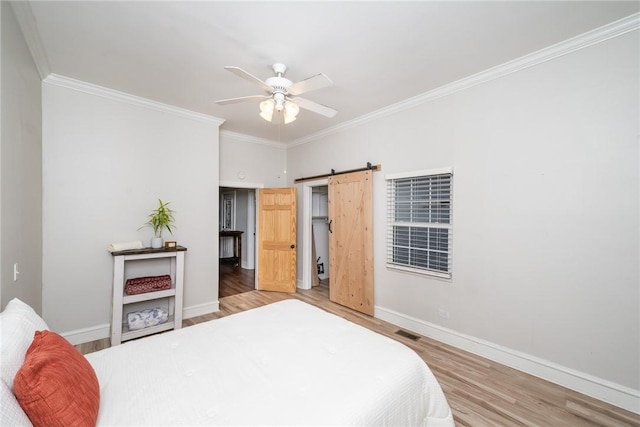 bedroom with ceiling fan, ornamental molding, wood-type flooring, and a barn door