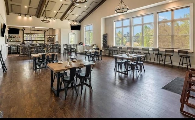 dining space featuring an inviting chandelier, dark wood-type flooring, high vaulted ceiling, and indoor bar