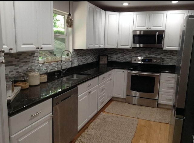 kitchen with tasteful backsplash, sink, white cabinets, stainless steel appliances, and light wood-type flooring