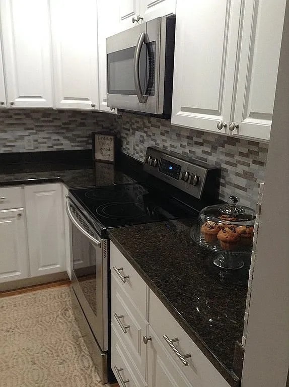 kitchen featuring white cabinetry, appliances with stainless steel finishes, dark stone counters, and backsplash