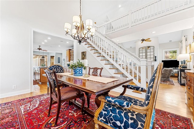 dining area with hardwood / wood-style flooring, ceiling fan with notable chandelier, and a towering ceiling