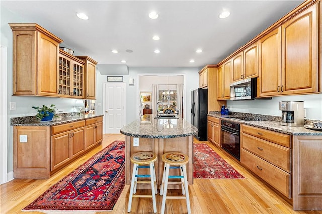 kitchen with sink, stone counters, a kitchen breakfast bar, a center island, and black appliances