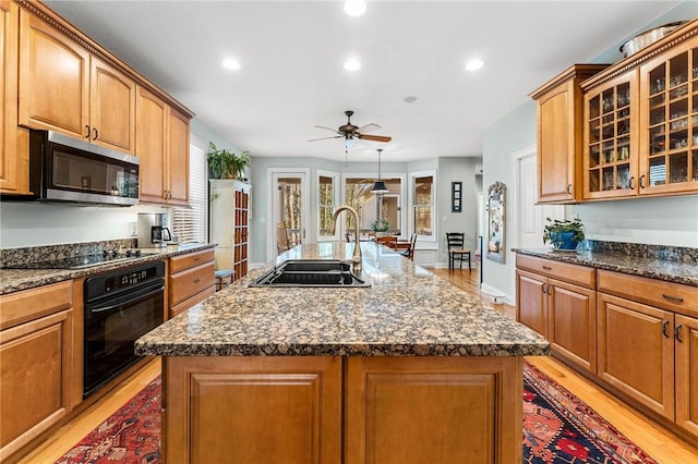 kitchen with sink, black appliances, an island with sink, and light wood-type flooring