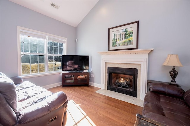 living room with a tiled fireplace, vaulted ceiling, and wood-type flooring