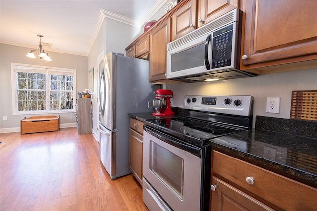 kitchen featuring dark stone countertops, hanging light fixtures, ornamental molding, and appliances with stainless steel finishes