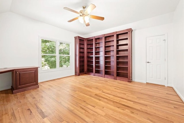 empty room with built in desk, lofted ceiling, light wood-style flooring, ceiling fan, and baseboards