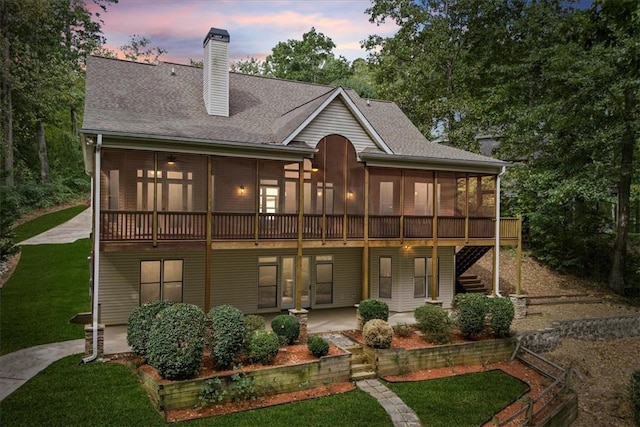 back of property with a patio, a shingled roof, a sunroom, stairway, and a chimney