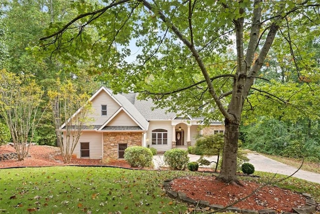 view of front of property featuring stone siding, a front lawn, and roof with shingles