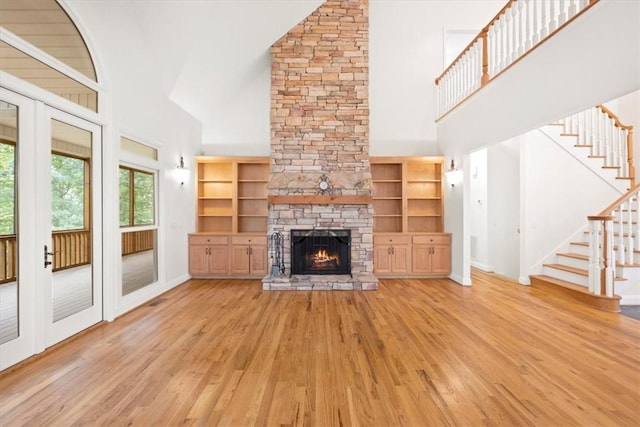 unfurnished living room featuring stairs, high vaulted ceiling, a fireplace, and wood finished floors