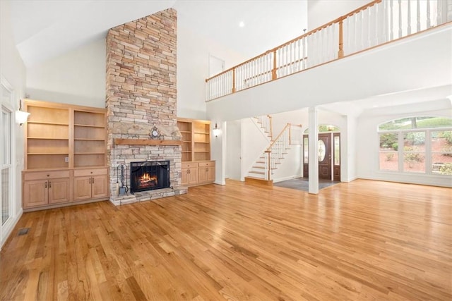 unfurnished living room with light wood-type flooring, a fireplace, stairway, and a high ceiling