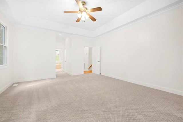 unfurnished room featuring ceiling fan, light colored carpet, baseboards, a tray ceiling, and crown molding