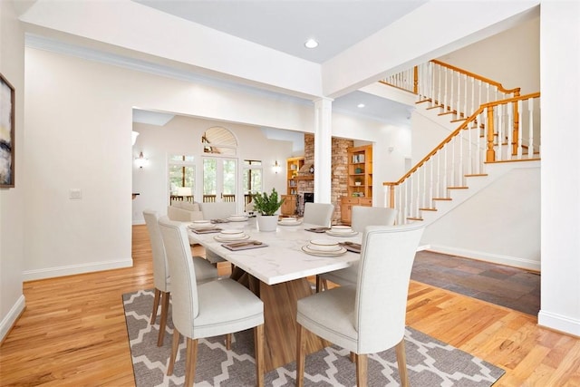 dining room featuring light wood-style floors, a stone fireplace, stairway, and baseboards