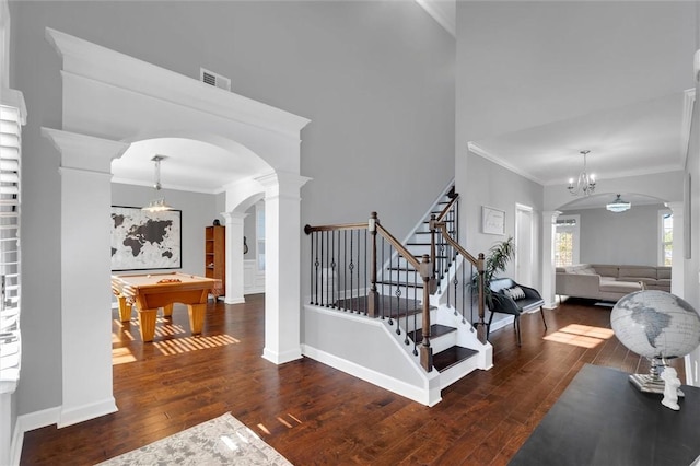 stairway with crown molding, wood-type flooring, decorative columns, and a notable chandelier