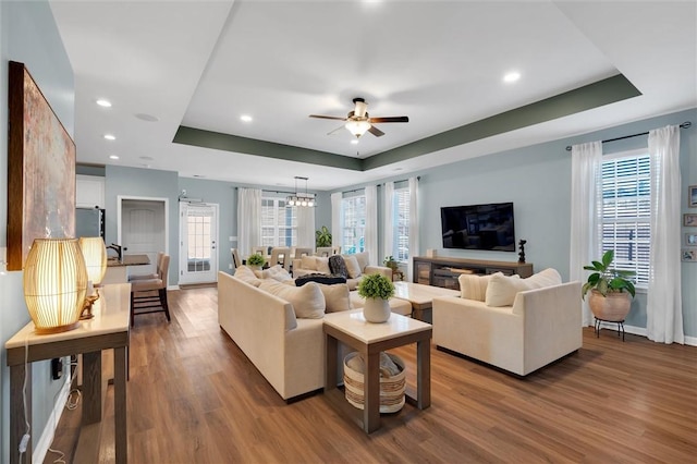 living room featuring a raised ceiling, wood-type flooring, and ceiling fan with notable chandelier