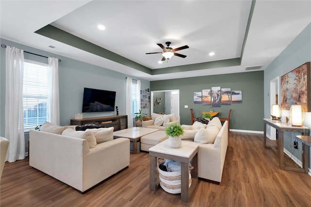 living room with hardwood / wood-style flooring, ceiling fan, and a tray ceiling