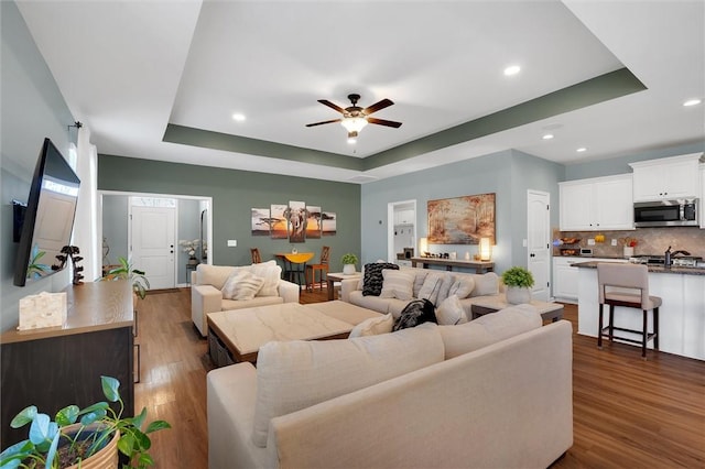 living room featuring dark hardwood / wood-style flooring, a raised ceiling, and ceiling fan