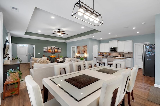 dining room featuring hardwood / wood-style flooring, ceiling fan, and a tray ceiling