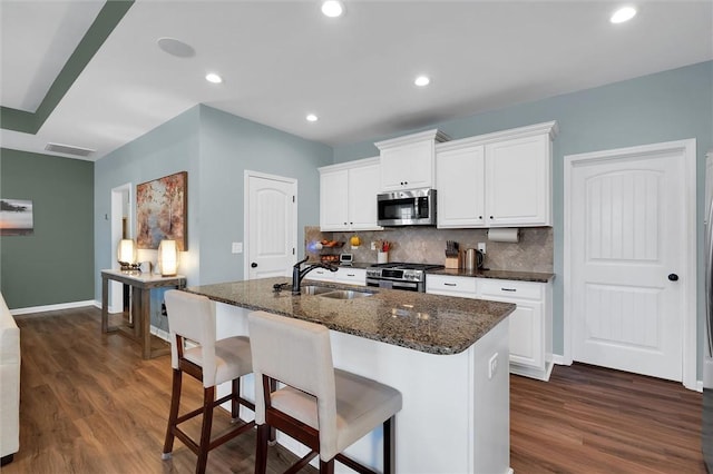 kitchen featuring sink, appliances with stainless steel finishes, white cabinetry, an island with sink, and dark stone counters