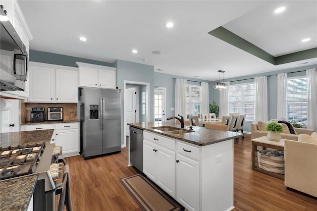 kitchen featuring pendant lighting, sink, white cabinets, stainless steel appliances, and a center island with sink