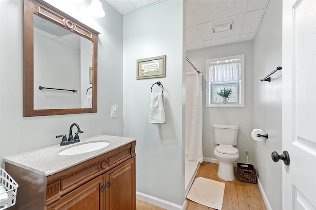 bathroom with a paneled ceiling, vanity, wood-type flooring, curtained shower, and toilet