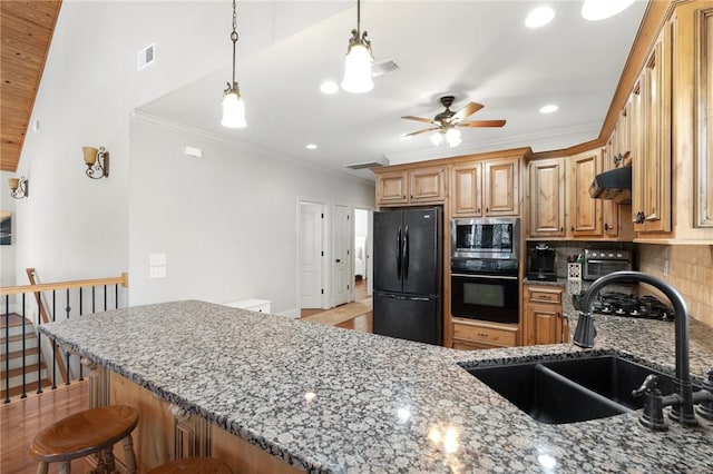 kitchen with stone countertops, sink, black appliances, and a kitchen bar