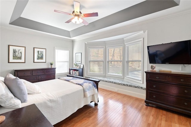 bedroom featuring ceiling fan, ornamental molding, a tray ceiling, and light wood-type flooring