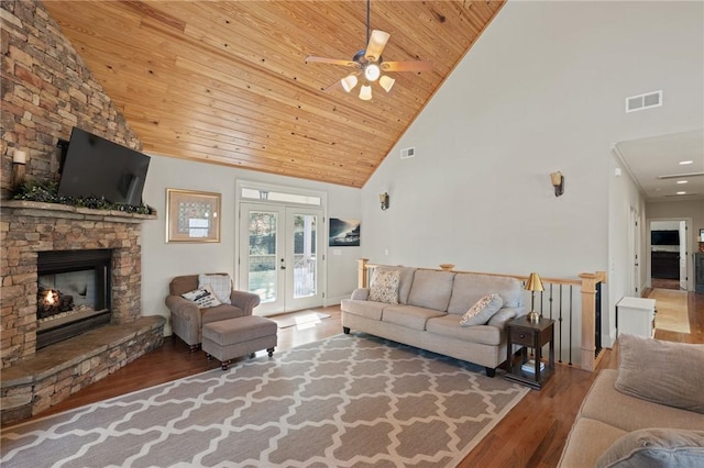 living room with a stone fireplace, hardwood / wood-style floors, high vaulted ceiling, wooden ceiling, and french doors