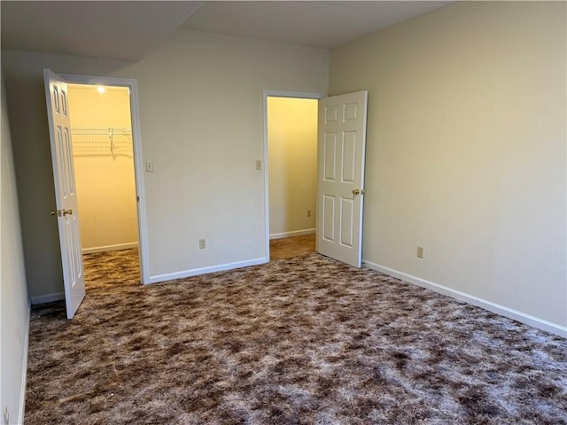 unfurnished bedroom with dark colored carpet, a spacious closet, and a closet