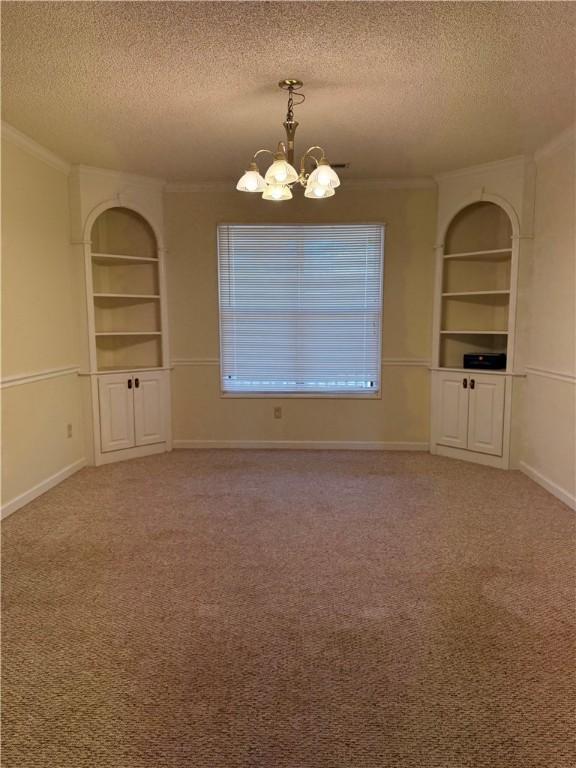 carpeted spare room with ornamental molding, a textured ceiling, and built in shelves