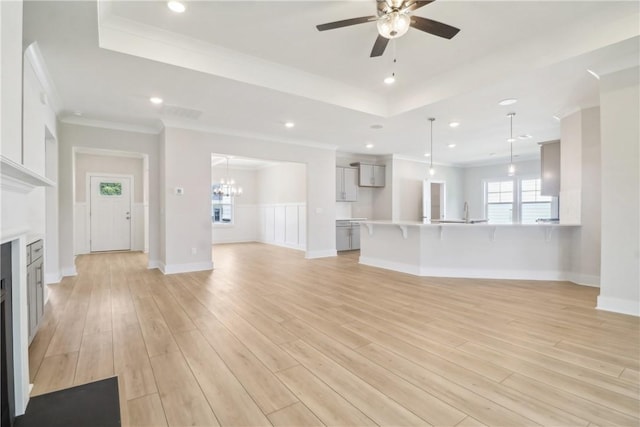 unfurnished living room with crown molding, a tray ceiling, ceiling fan with notable chandelier, and light hardwood / wood-style flooring