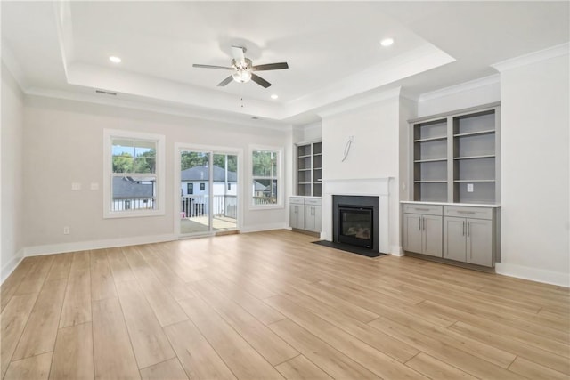 unfurnished living room with ceiling fan, crown molding, light wood-type flooring, and a tray ceiling