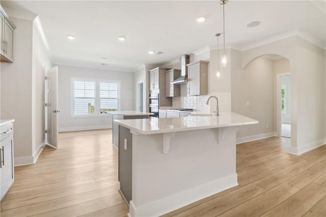 kitchen with gray cabinets, tasteful backsplash, hanging light fixtures, wall chimney range hood, and light wood-type flooring