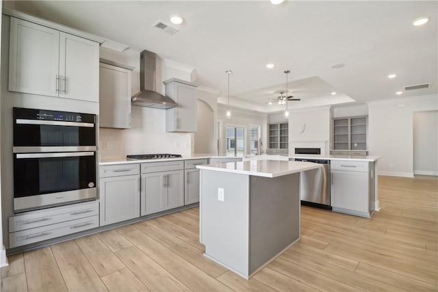 kitchen with appliances with stainless steel finishes, kitchen peninsula, a kitchen island, and wall chimney range hood