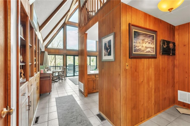 hallway with light tile patterned flooring, high vaulted ceiling, and wooden walls