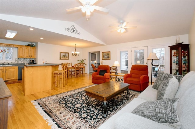 living room featuring sink, ceiling fan with notable chandelier, vaulted ceiling, and light hardwood / wood-style floors