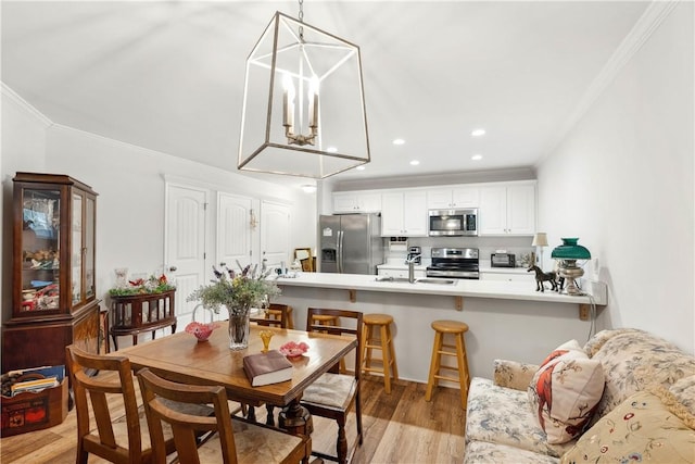 dining area featuring an inviting chandelier, sink, crown molding, and light hardwood / wood-style floors