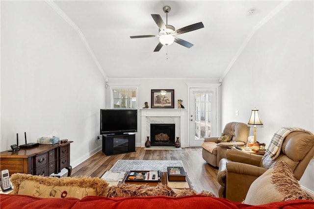 living room with crown molding, a fireplace, ceiling fan, and light wood-type flooring