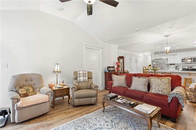 living room featuring ceiling fan with notable chandelier, vaulted ceiling, and light wood-type flooring