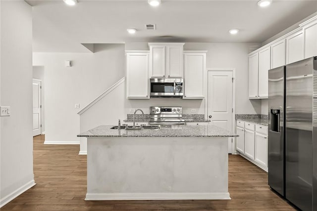 kitchen featuring white cabinetry, sink, stainless steel appliances, light stone countertops, and a center island with sink