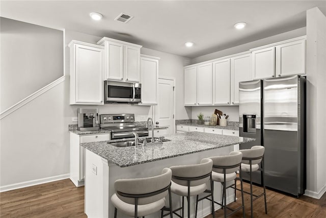 kitchen featuring stainless steel appliances, a breakfast bar area, white cabinets, and light stone counters