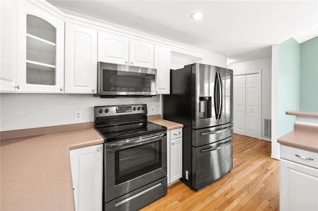 kitchen featuring glass insert cabinets, stainless steel appliances, light countertops, light wood-style floors, and white cabinetry